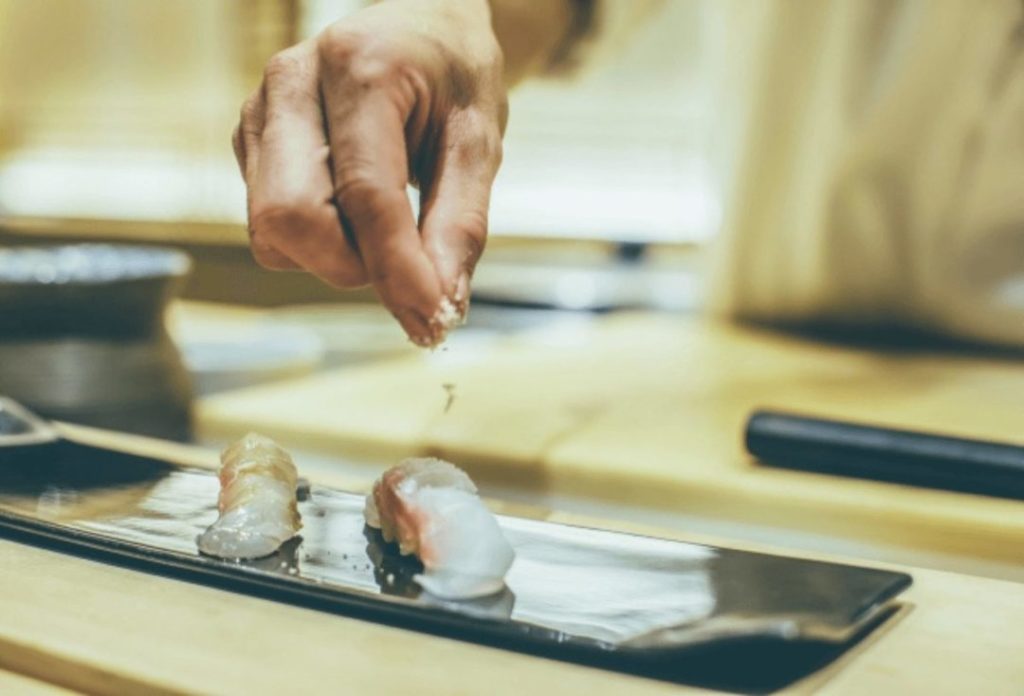 A sushi chef sprinkling salt onto a sushi